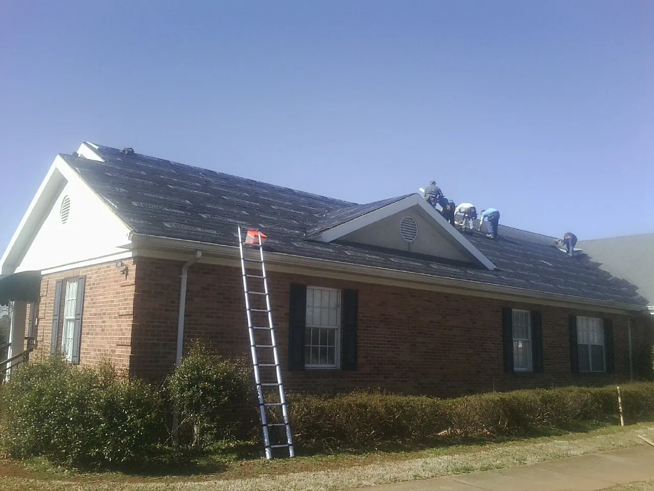 Crew tearing shingles off a brick ranch roof with a ladder set — Emergency Roof Repair work by our crew in Atlanta